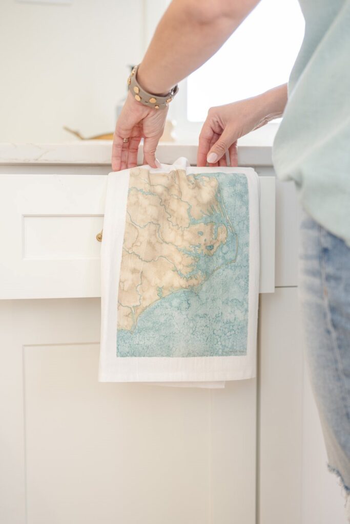 artist holds tea towel adorned with her coastal watercolor map artwork in Wilmington, North Carolina