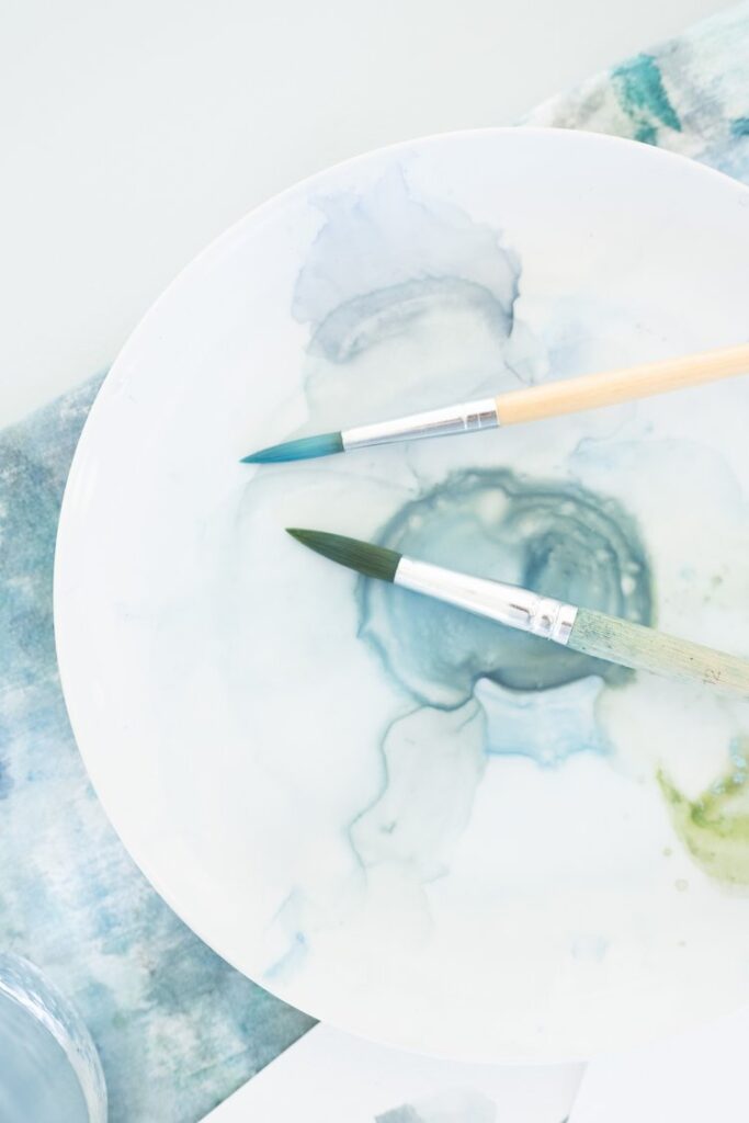 two paintbrushes rest on a white color palette with blotches of blue paint