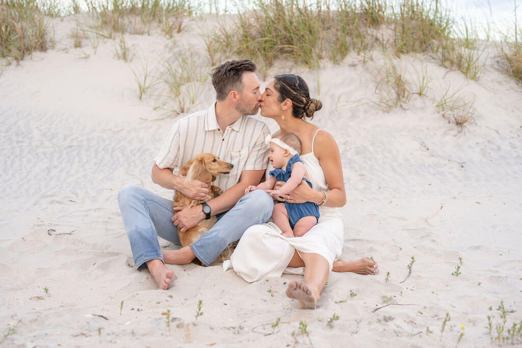 Family enjoying a sweet moment with infant and family dog in the dunes on North Topsail Beach in North Carolina.