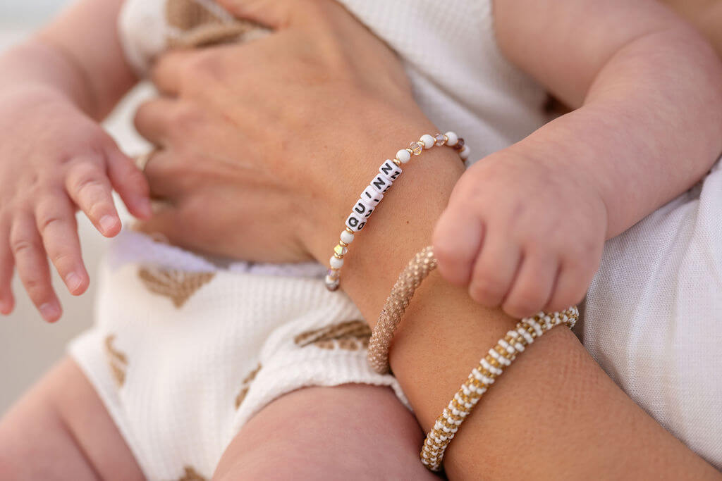 Baby girl touches the sentimental bracelets on her mom's arm. 