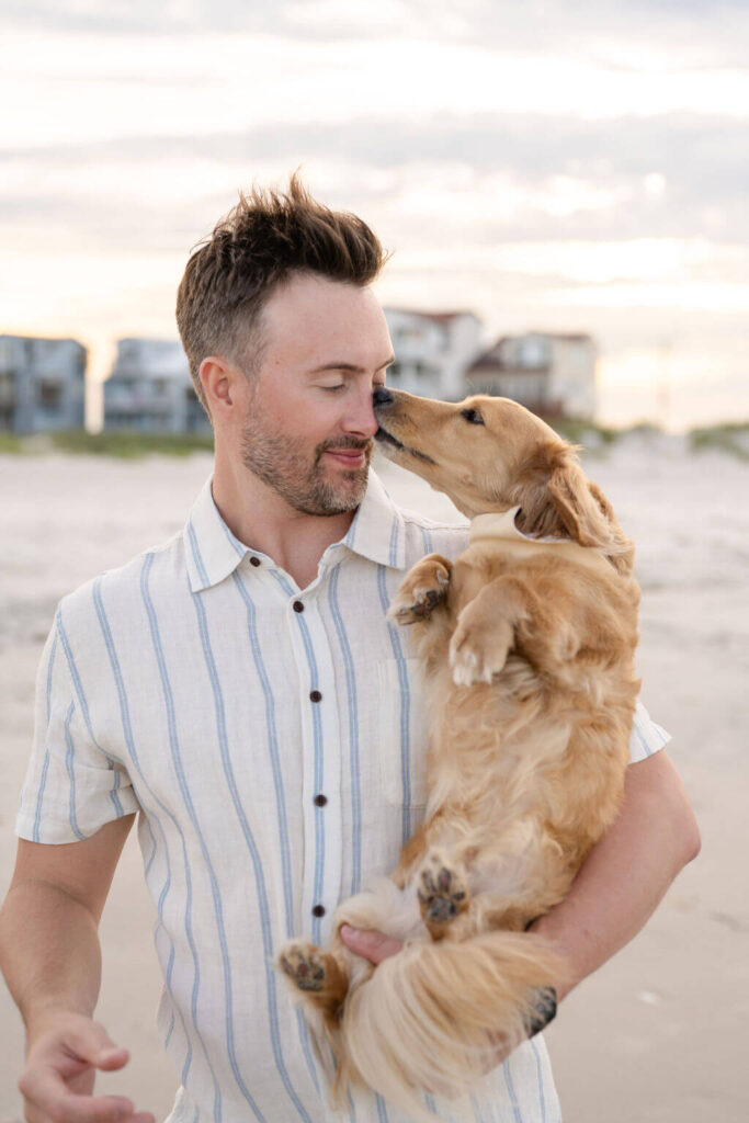 Family dog steals a kiss from human dad on the beach in North Topsail, North Carolina.