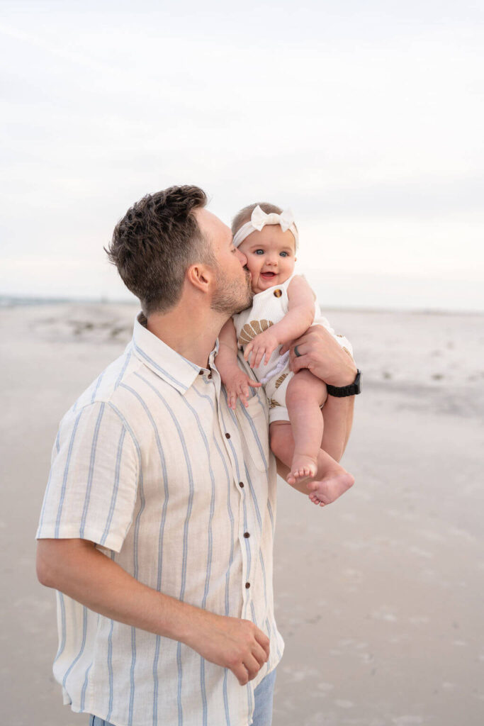 Dad stealing a kiss from his cute baby girl on the beach in North Carolina.