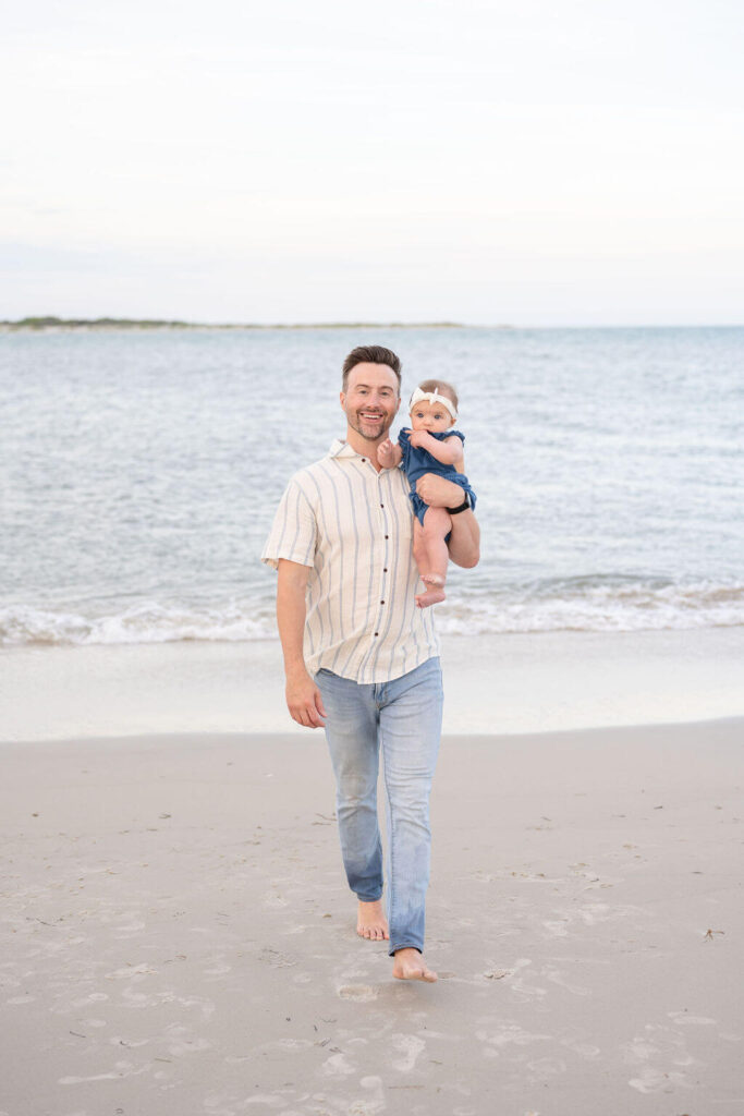 Dad happily walking on North Topsail Beach with his baby girl in his arms.