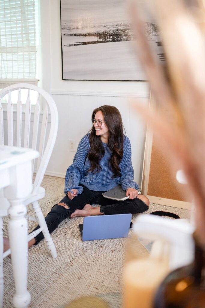 Annie sitting on the dining room floor gazing left holding a pen and notebook with an ipad set out