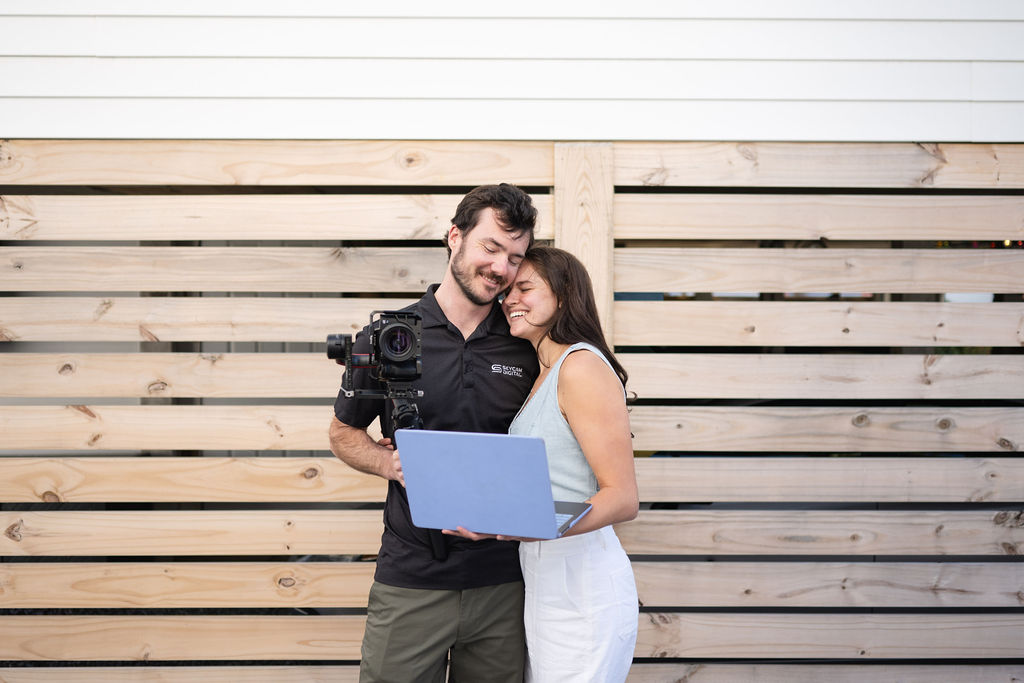 couple embrace as woman hold laptop and man holds camera in Wilmington, North Carolina