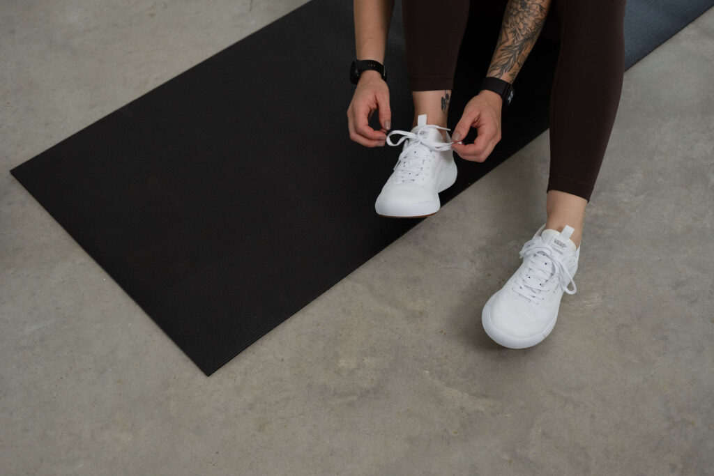 A branding photoshoot for a female fitness and health coach tying shoe on a yoga mat.
