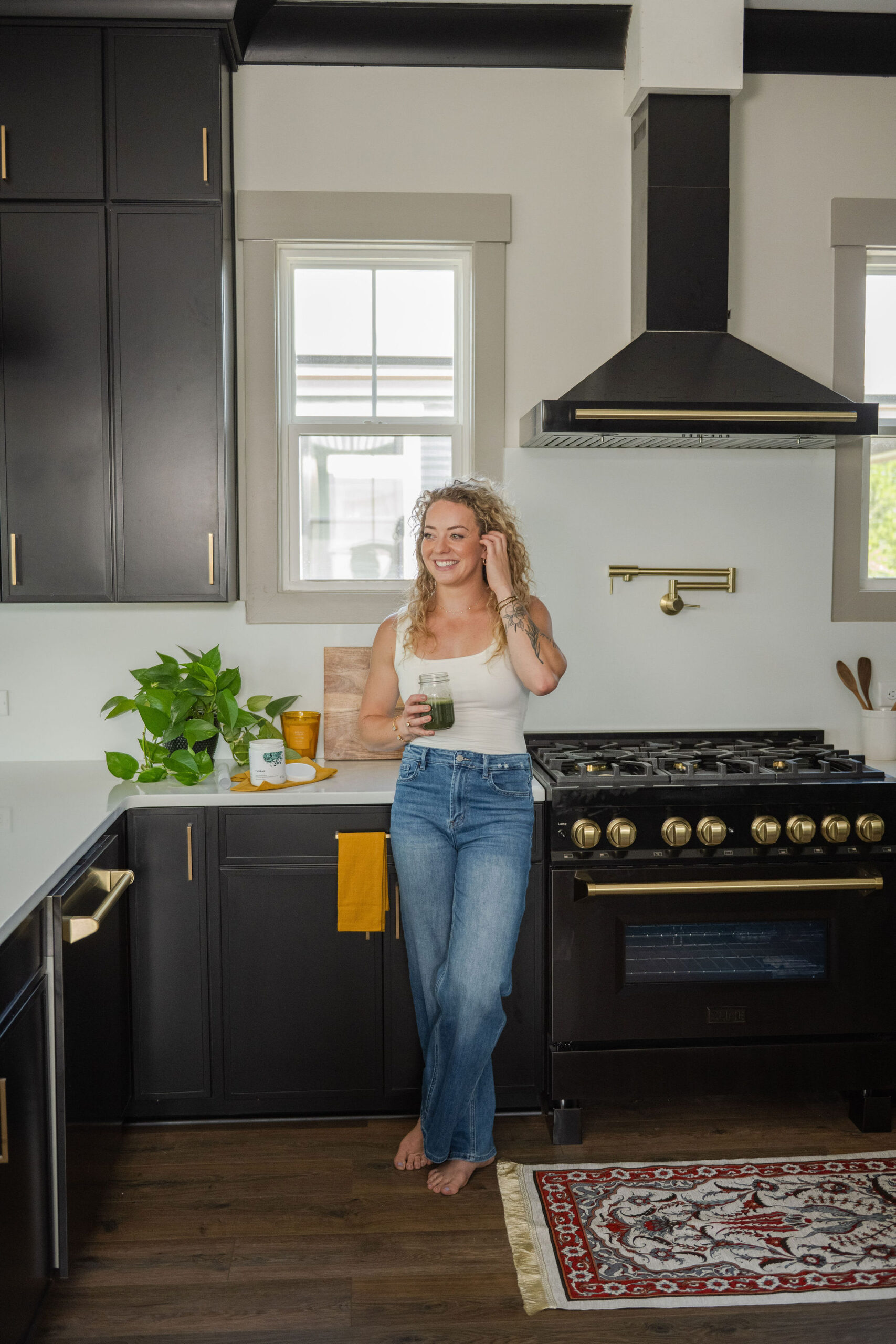 Colleen standing in kitchen wearing white tank and jeans