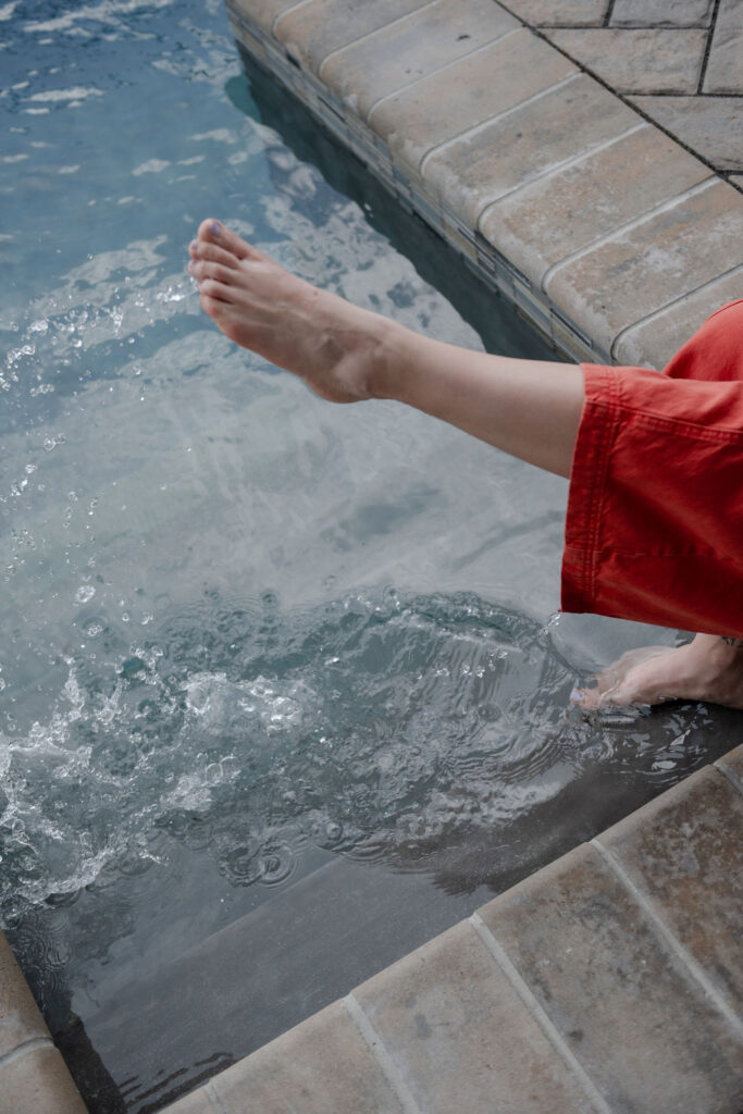 A branding photoshoot for a female fitness and health coach sitting with her toes in a pool.