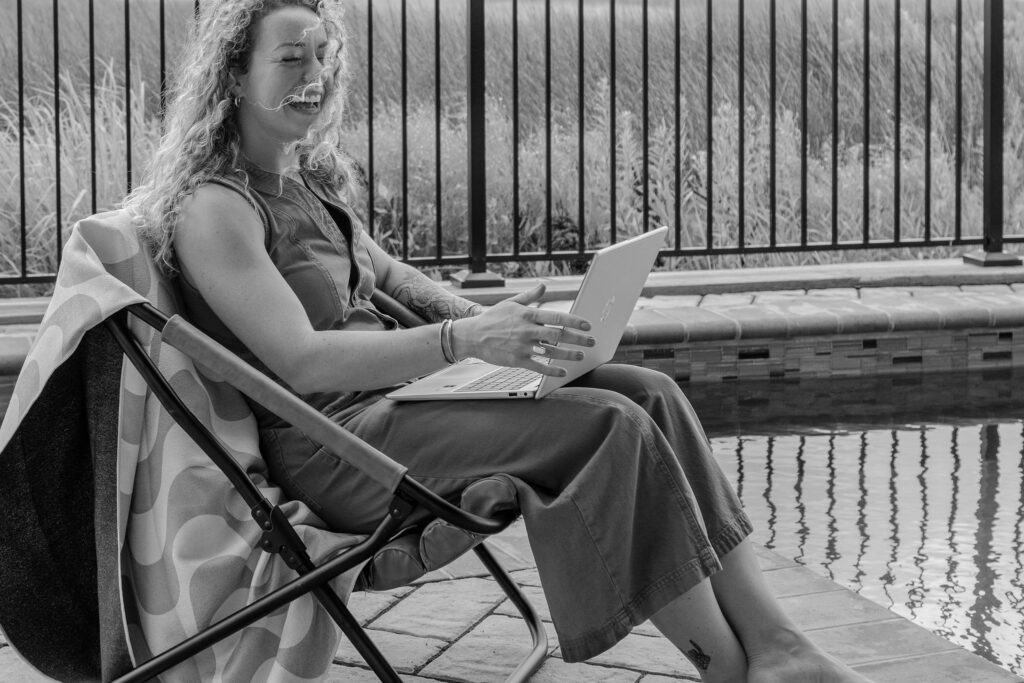 A branding photoshoot for a female fitness and health coach sitting by the pool with her laptop.